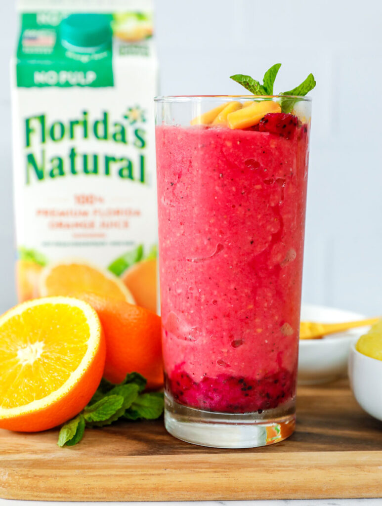 Un vaso alto de batido tropical hecho con jugo de naranja.