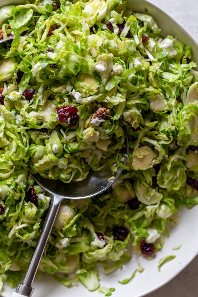 Primer plano de ensalada de coles de Bruselas afeitadas con arándanos, queso de cabra, nueces y aderezo de arce