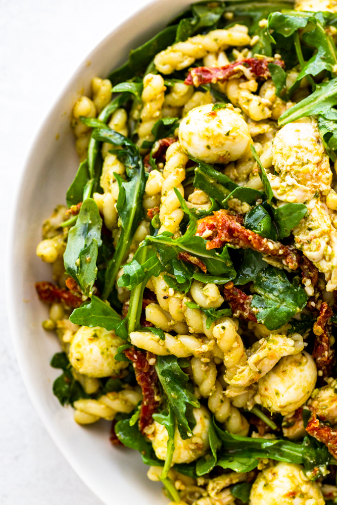 Primer plano de ensalada de pasta con pesto de pollo en un tazón blanco