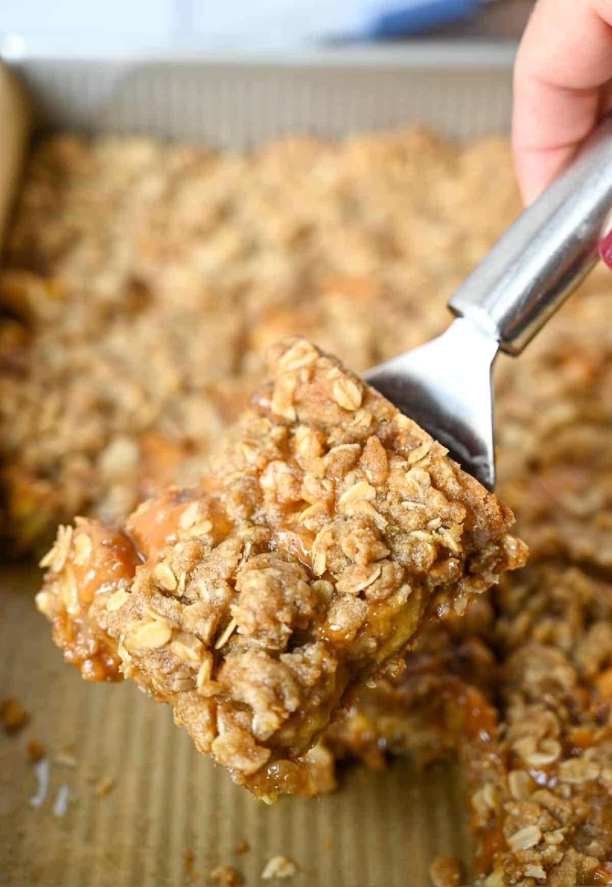 Una espátula de metal que recoge un cuadrado de crumble de manzana.