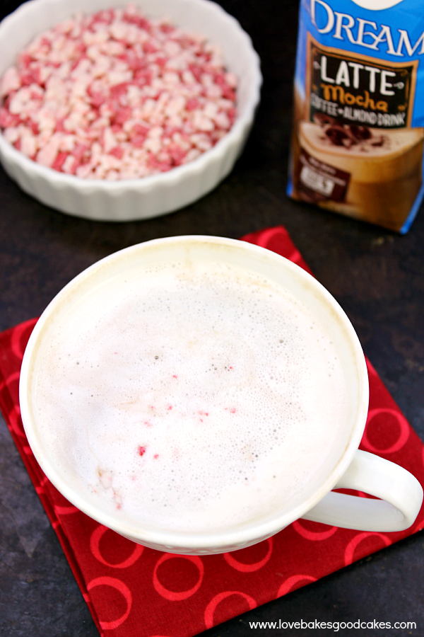 Leche de menta sin lácteos: ¡sabe como una bebida de café cara! #DREAMLatte #anuncio Leche de menta sin lácteos en un vaso con un bol de trozos de menta.