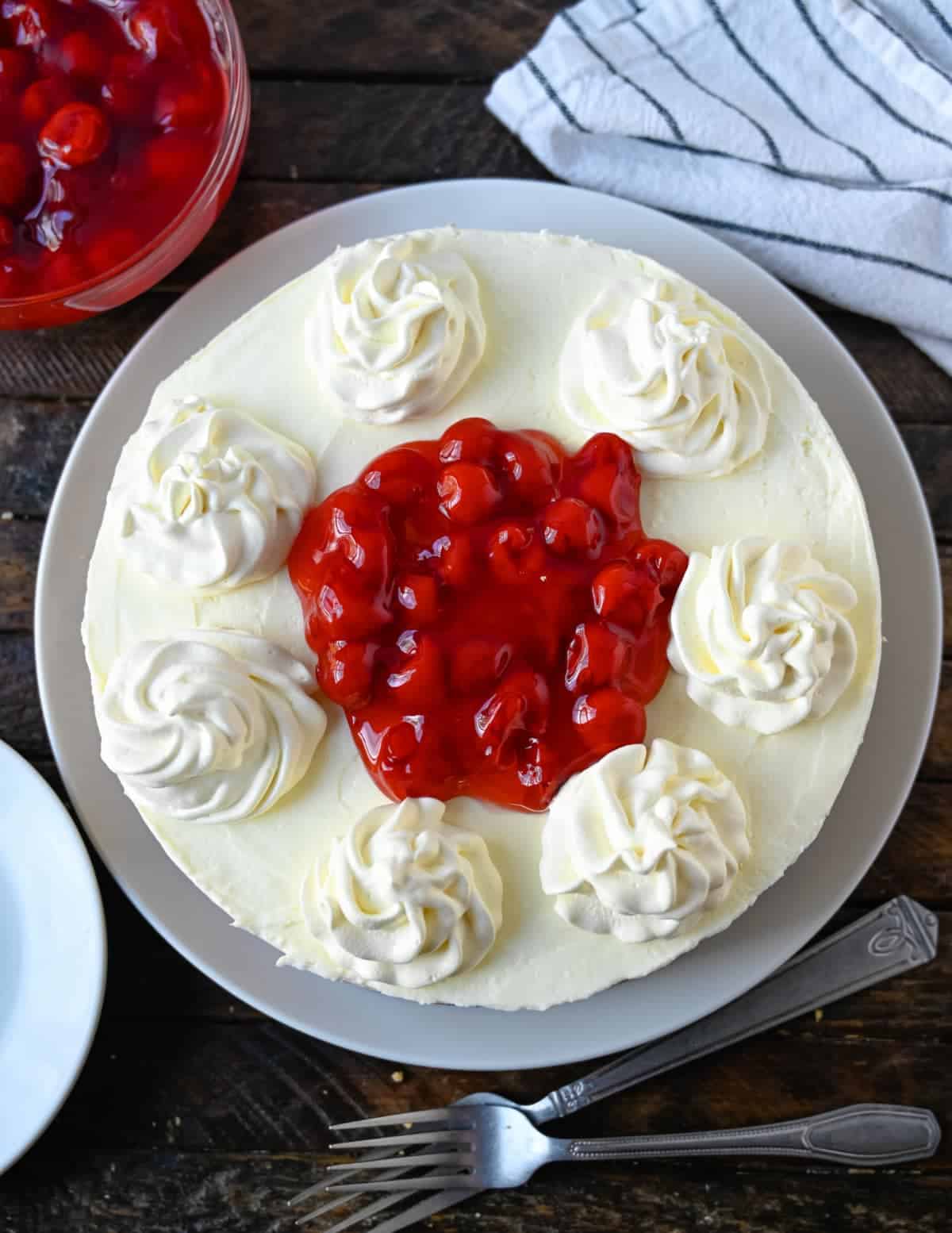 Una tarta de queso entera sin hornear con crema batida y cerezas encima.