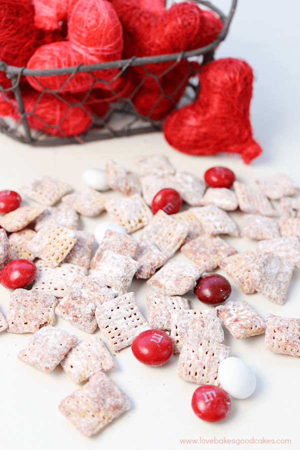 ¡Estos Muddy Buddies de Red Velvet son rápidos, fáciles y deliciosos! ¡A tu familia le encantará el toque de temporada en una delicia clásica! Red Velvet Muddy Buddies sobre una mesa con corazones rojos.