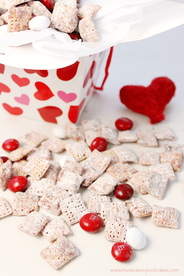 ¡Estos Muddy Buddies de Red Velvet son rápidos, fáciles y deliciosos! ¡A tu familia le encantará el toque de temporada en una delicia clásica! Red Velvet Muddy Buddies sobre una mesa con una caja llena.