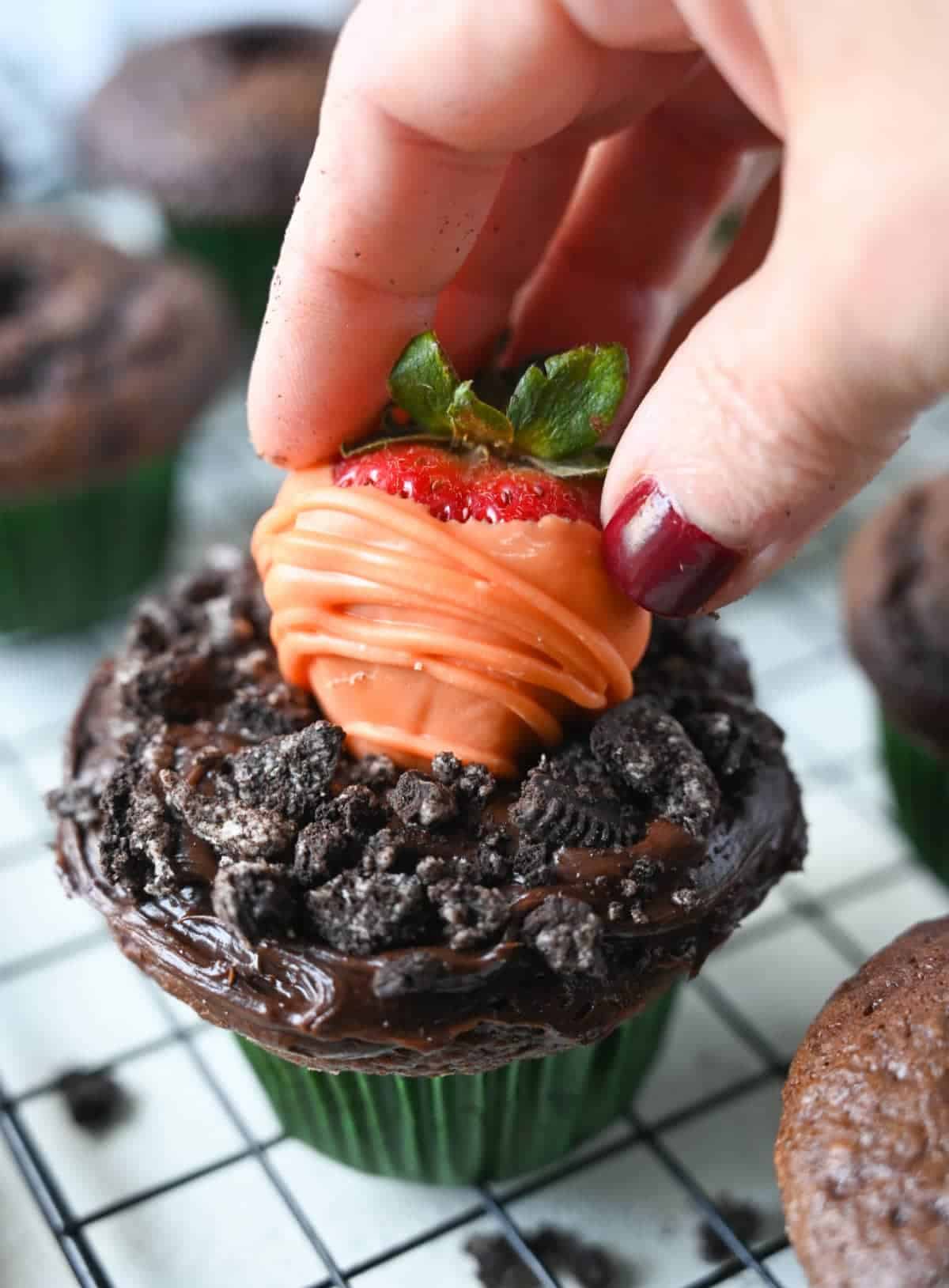 Una fresa bañada en chocolate naranja se coloca justo encima del cupcake de chocolate.