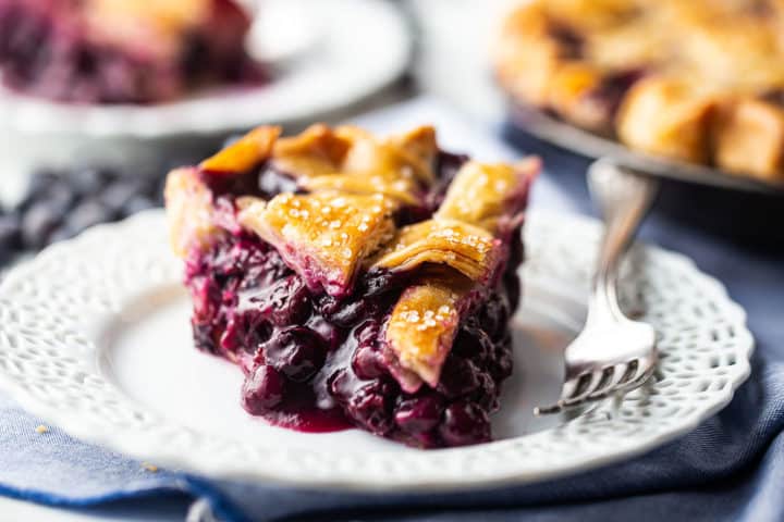 Primer plano de la receta de relleno de tarta de arándanos, horneada en una masa de tarta desmenuzada y servida en un plato blanco con una servilleta azul.