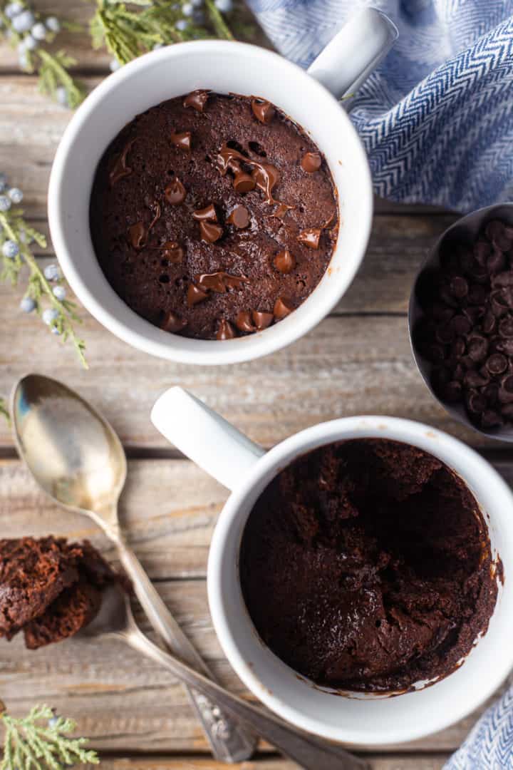 Imagen aérea de dos pasteles de chocolate en un vaso servido sobre una superficie de madera envejecida con cucharas de plata antiguas.