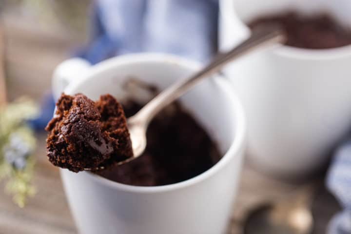 Primer plano de una cuchara de pastel de taza de chocolate que descansa sobre el borde de una taza de café de cerámica blanca.