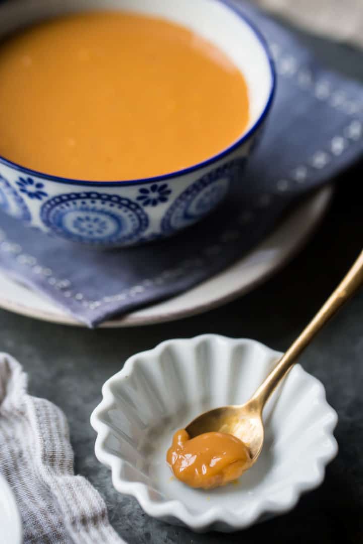 Una cucharada de dulce de leche en un platillo blanco, con un tazón más grande de dulce de leche al fondo.