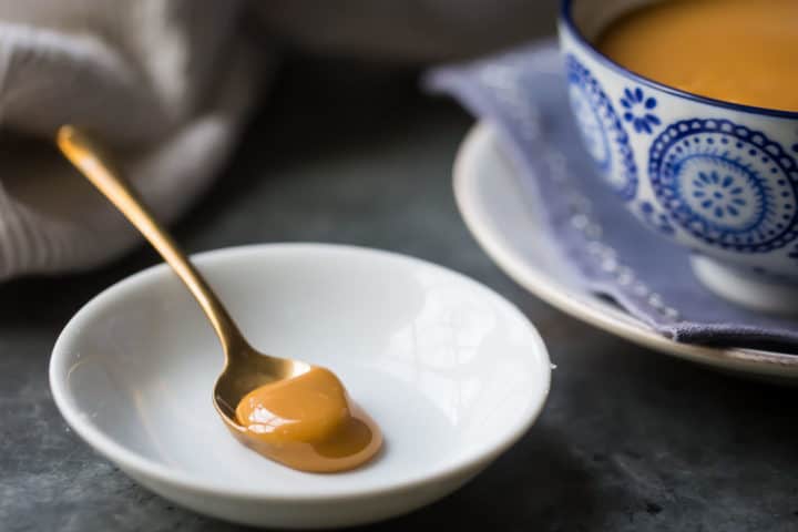 Cuchara dorada de dulce de leche de caramelo en un plato blanco con un cuenco azul estampado en el fondo.