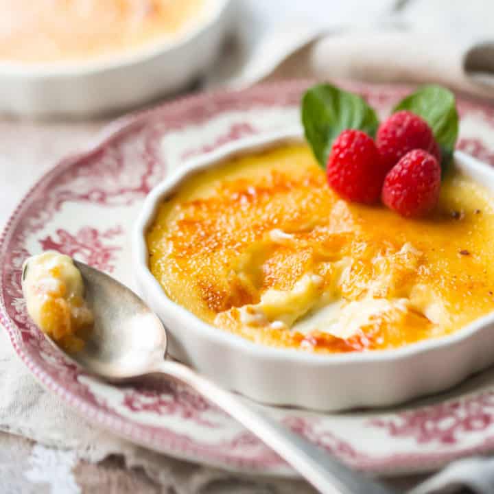 Creme brulee en un plato poco profundo sobre un plato vintage, con guarnición de frambuesa fresca y menta.