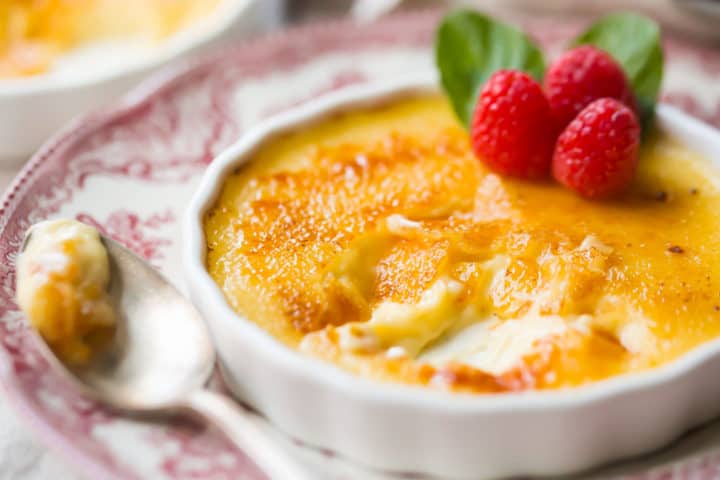 Primer plano de un creme brulee parcialmente comido, con una parte superior de azúcar crujiente y una crema suave debajo.