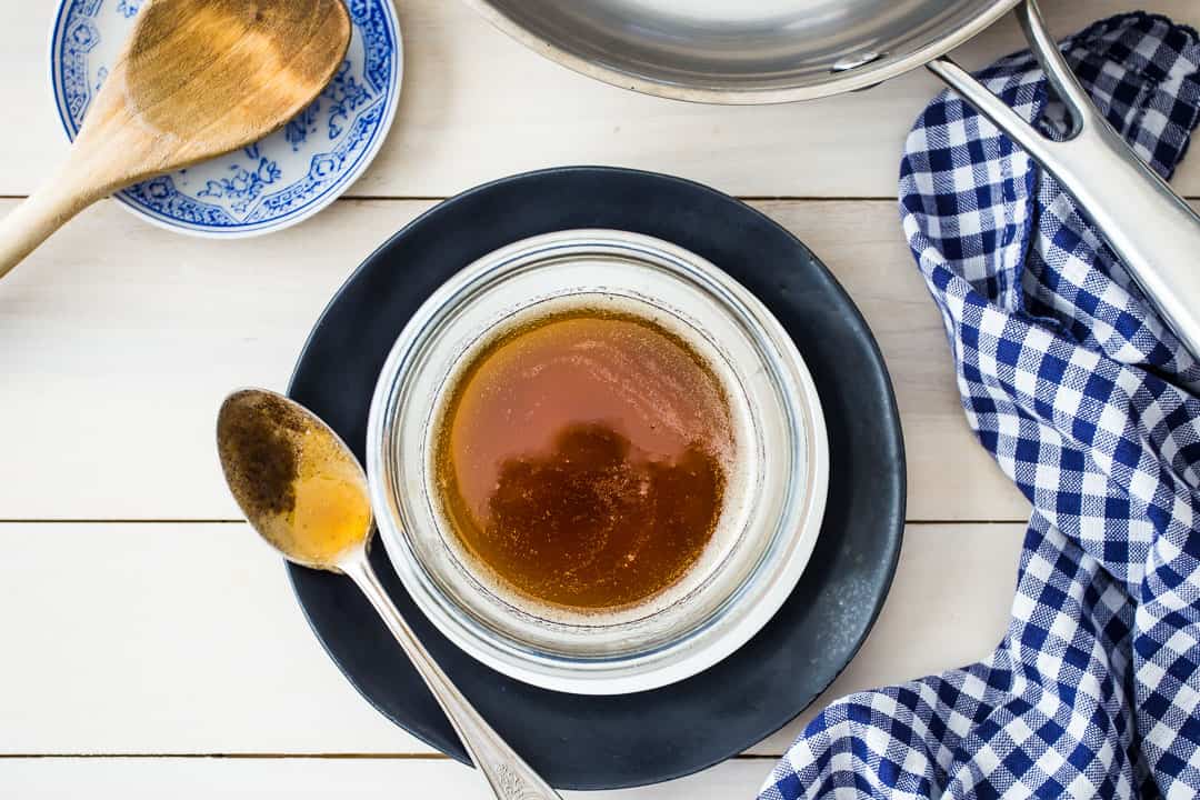 Imagen superior de un tazón de mantequilla marrón, con una cuchara de plata, una sartén de acero inoxidable y una servilleta azul a cuadros.