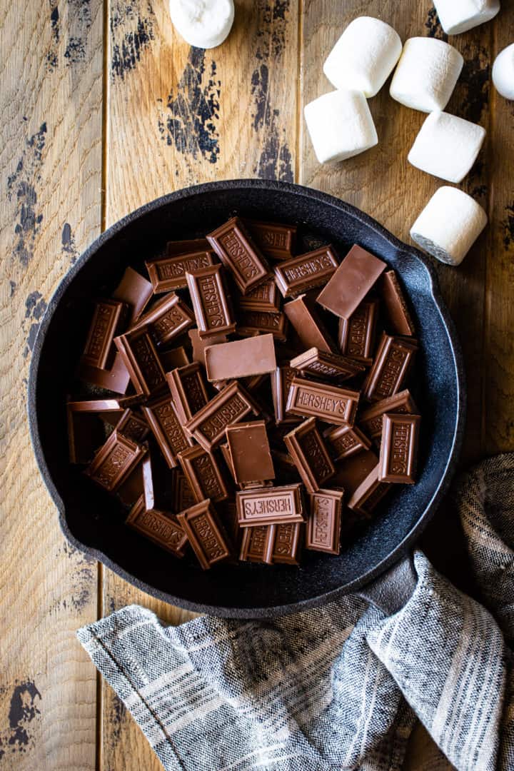 Barras de chocolate con leche, trituradas en trozos pequeños y extendidas en el fondo de una sartén de hierro.