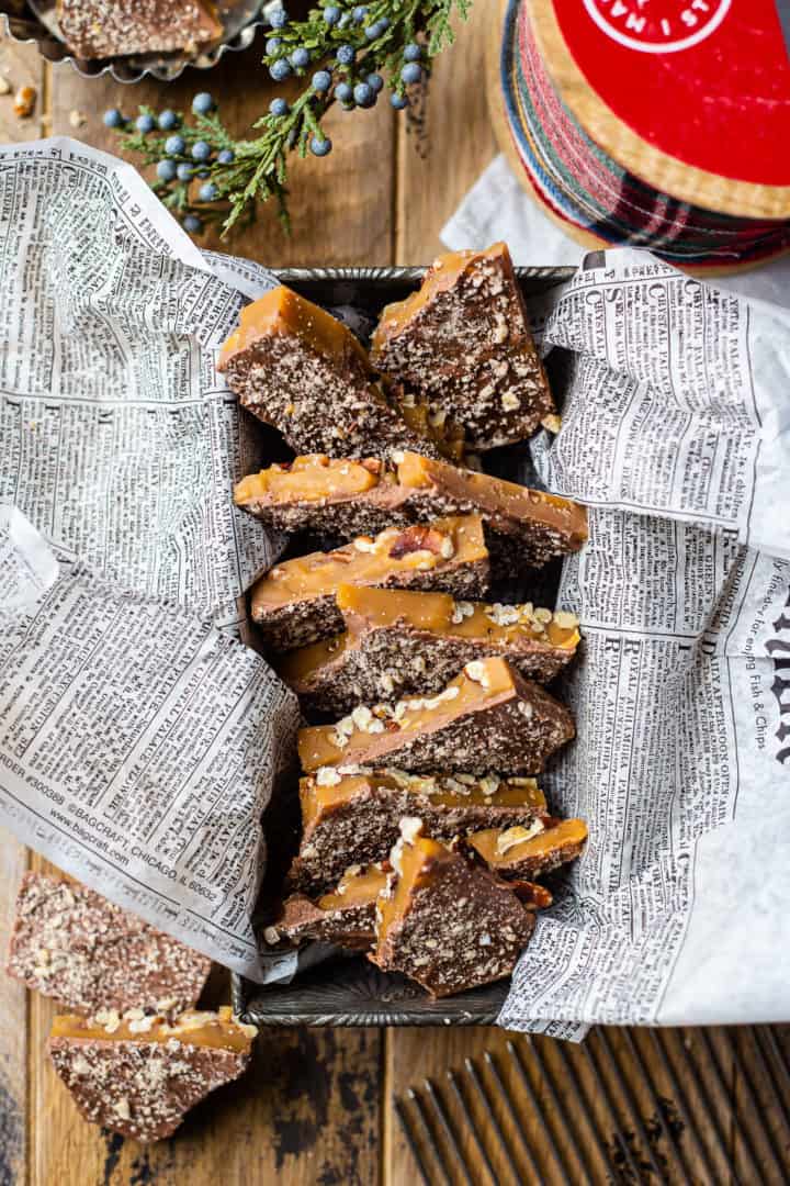 Fotografía cenital de gruesos trozos de caramelo casero alineados en una vieja bandeja para hornear, rodeados de vegetación y cintas.