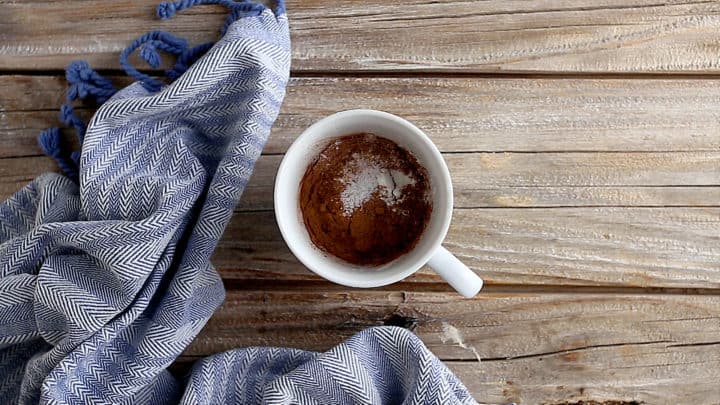 Ingredientes secos para bizcocho de chocolate en una taza de cerámica blanca.
