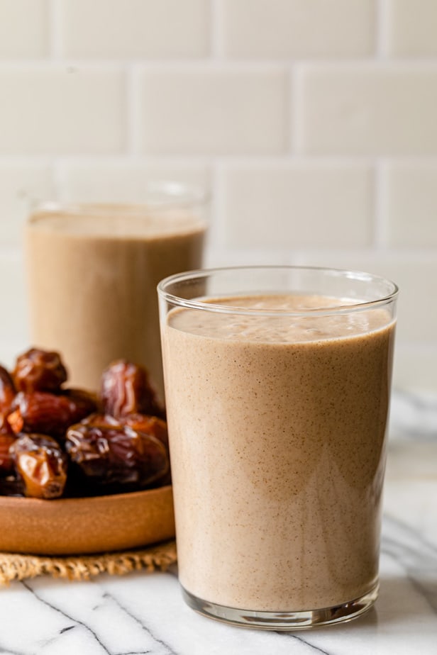 Un batido de dátiles en un vaso frente a un plato de dátiles