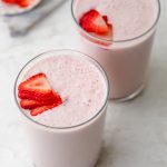 Dos vasos de batido de fresa y plátano cubierto con fresas