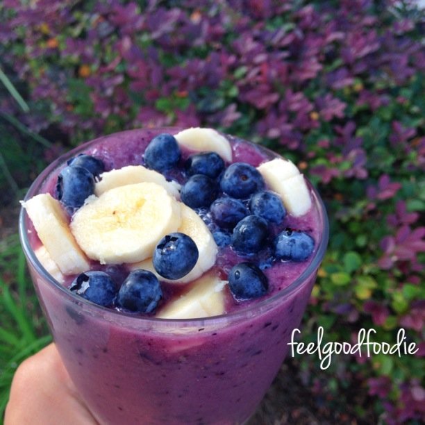 Smoothie saludable de plátano y arándanos hecho simplemente con arándanos, plátanos y leche de almendras y cubierto con bayas frescas para un refrigerio dulce y refrescante