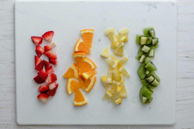 Cortar la fruta en fila: fresas, naranjas, limón y kiwi