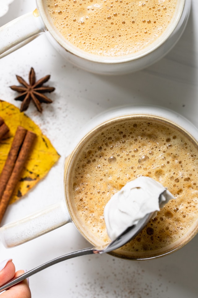 Fotografía cenital de una taza grande de leche y una cuchara con crema de coco batida encima