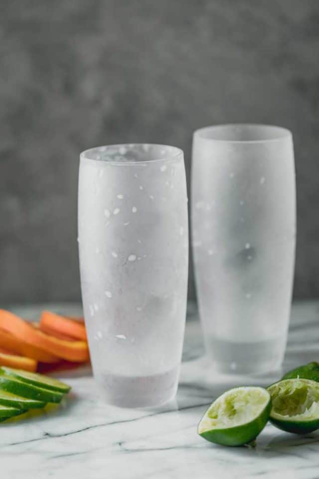 Dos vasos altos vacíos de vidrio esmerilado frío sobre un mostrador de mármol con rodajas de naranja y rodajas de limón alrededor