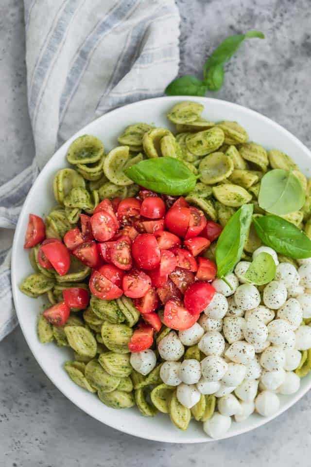 Tazón blanco grande y poco profundo de orecchiette cubierto con pesto cubierto con tomate, mozzarella y hojas de albahaca