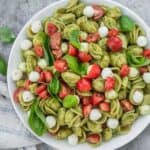 Esta ensalada de pasta caprese, el último plato de comida compartida de verano, está hecha con trozos de mozzarella perla, suculentos tomates cherry y se mezcla con un brillante pesto de perejil.