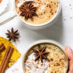 Tienda final de dos tazas de café con leche casero especiado con calabaza con una mano agarrando una de las tazas