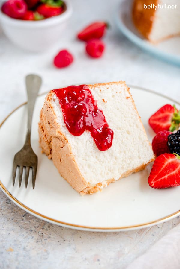Rebanada de pastel de ángel casero en plato blanco con tenedor y salsa de fresa