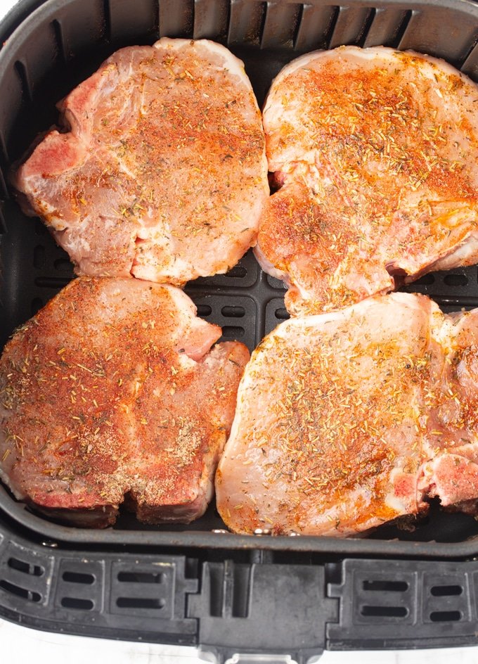 Chuletas de cerdo crudas cubiertas con condimentos en una canasta de freidora