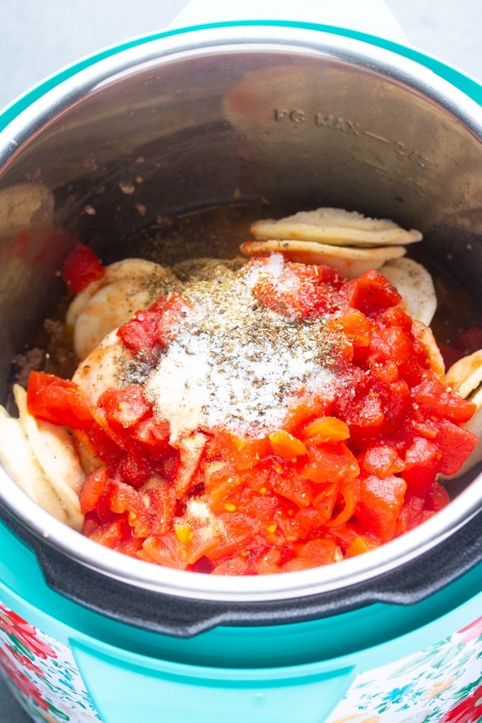 ingredientes con raviolis, tomate y condimentos en capas dentro de la olla instantánea